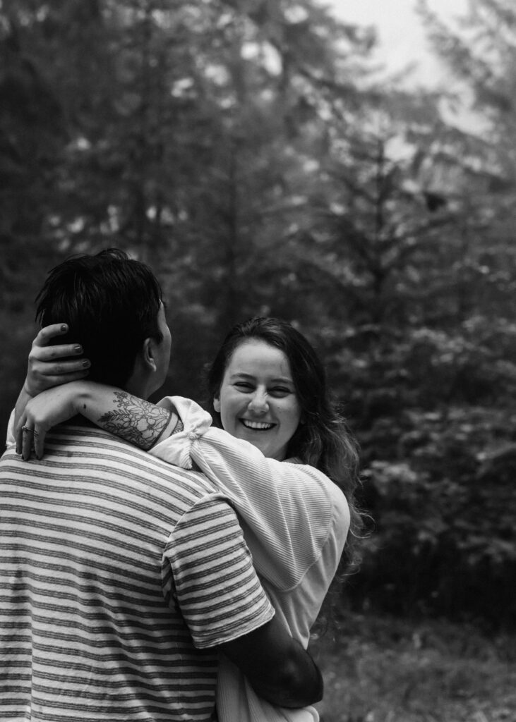 A smiling couple embraces while walking through the woods