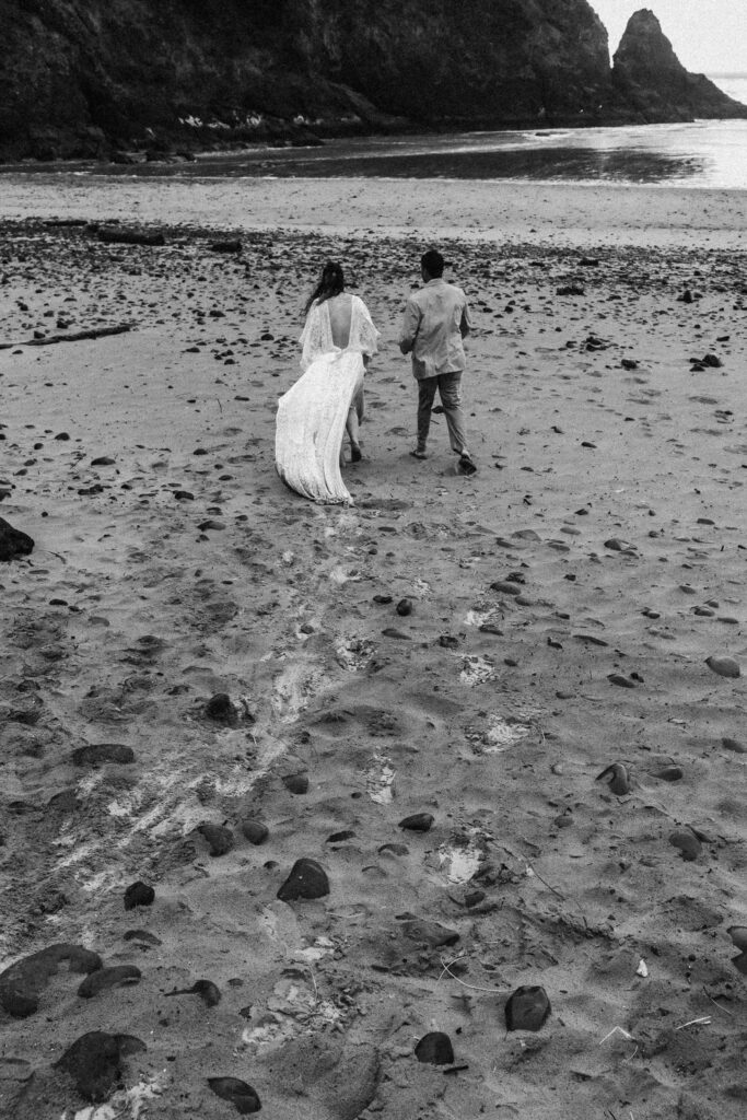 after their surfer wedding, a couple in their wedding attire explores a moody beach. their footsteps can be seen in the sannd.