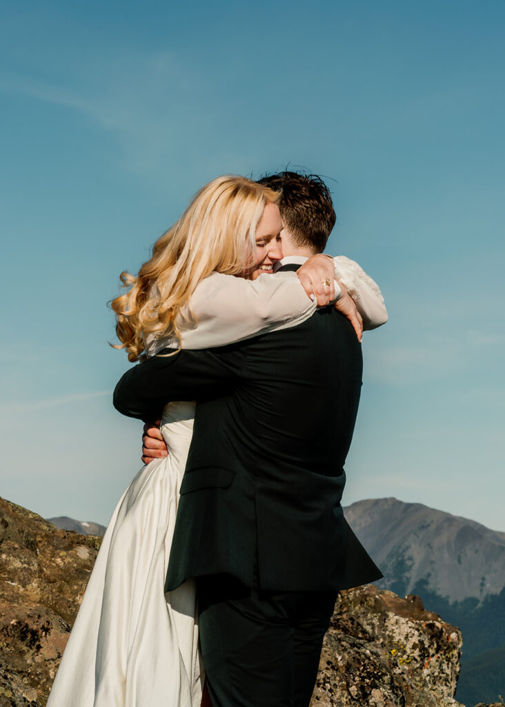 a bride and groom embrace during their Olympic Peninsula elopement. The sky above them is bright blue and the sun shines sweetly on them