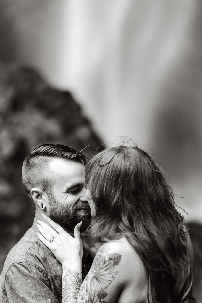 Couple in their wedding attire nuzzles each other in front of a waterfall during their waterfall elopement