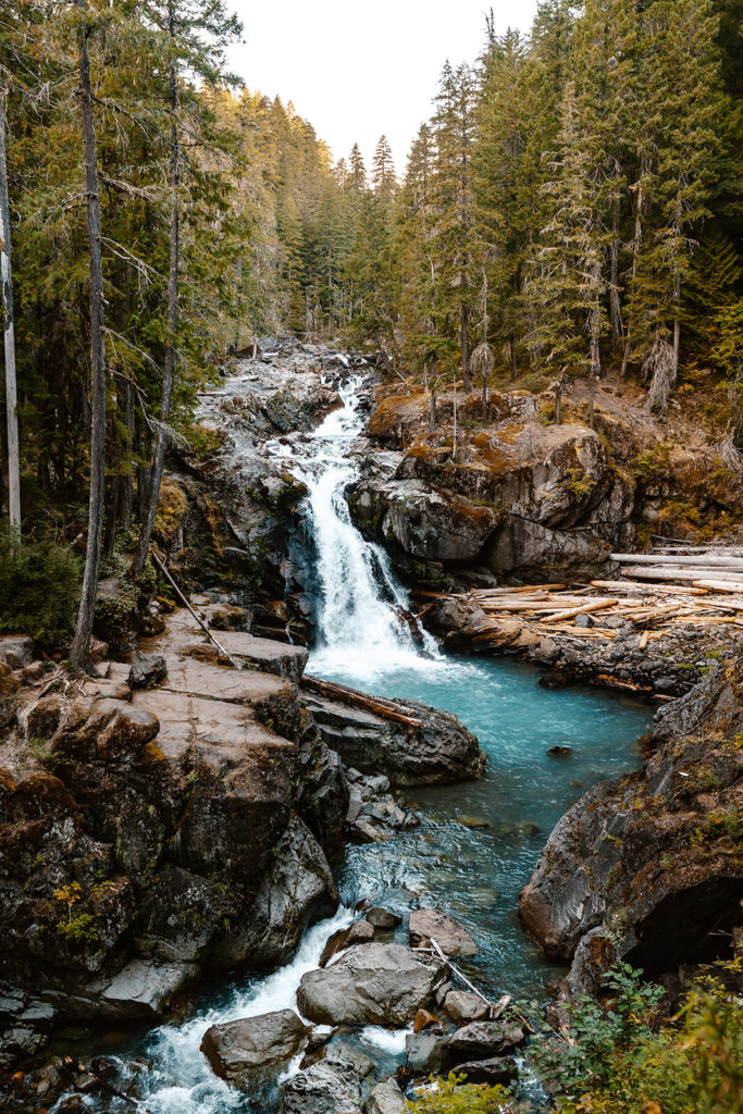 turquoise waterfall surrounded by pines and jagged cliffs, serving as the perfect location for a mt. rainier wedding