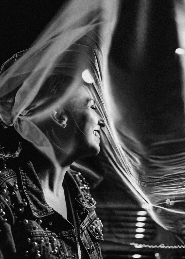 a bride wearing a jean jacket over her dress, smiles as her veil blows in the wind at the end of their elopement timeline