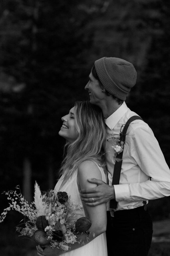 a black and white image of a bride and groom snuggling. A bride holds her bouquet, her groom holds her as they both smile broadly