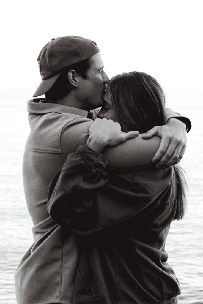 a couple embraces with gentle waves behind them during the morning of their coastal elopement