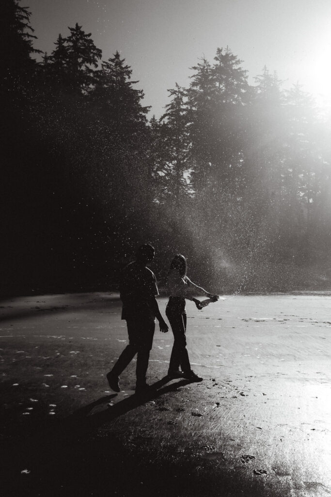 during the morning of their coastal elopement, a bride and groom pop a bottle of champagne on the beach  