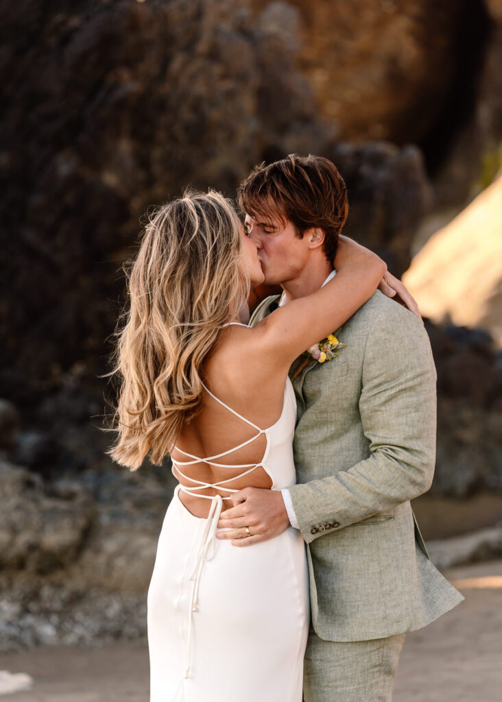 a couple kisses during their coastal elopement during sunset on a rocky beach