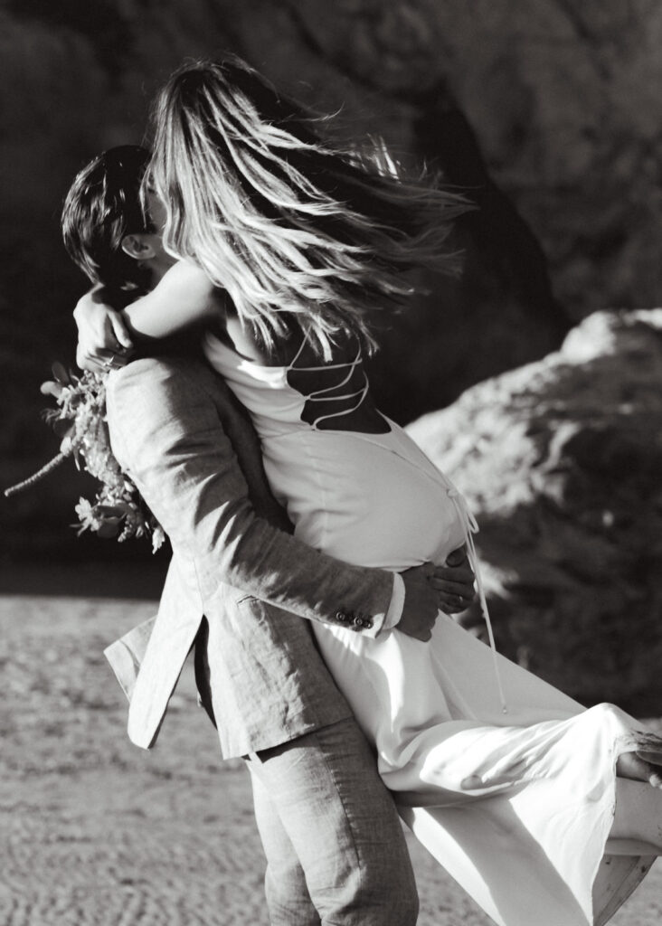 A black and white image of a bride and groom spinning during their coastal elopement. 