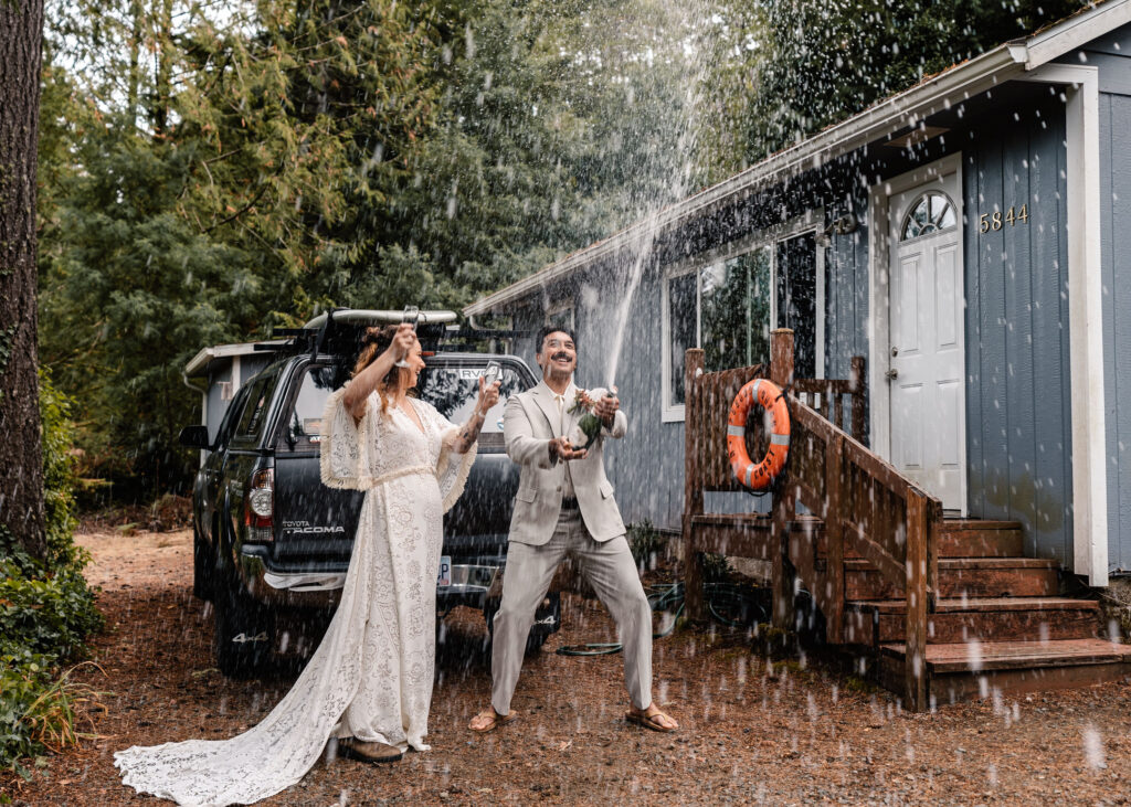 A couple in their wedding attire pop a bottle of champagne as they celebrate their surfer wedding