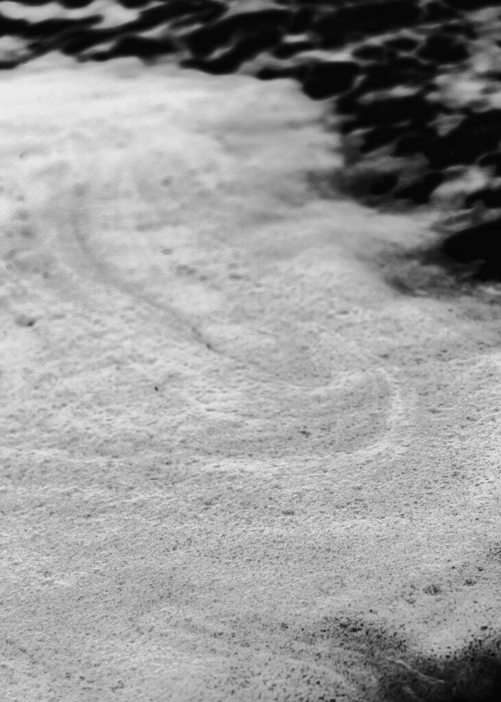 A black and white image of the texture of the sea foam witnessed during this surfer wedding