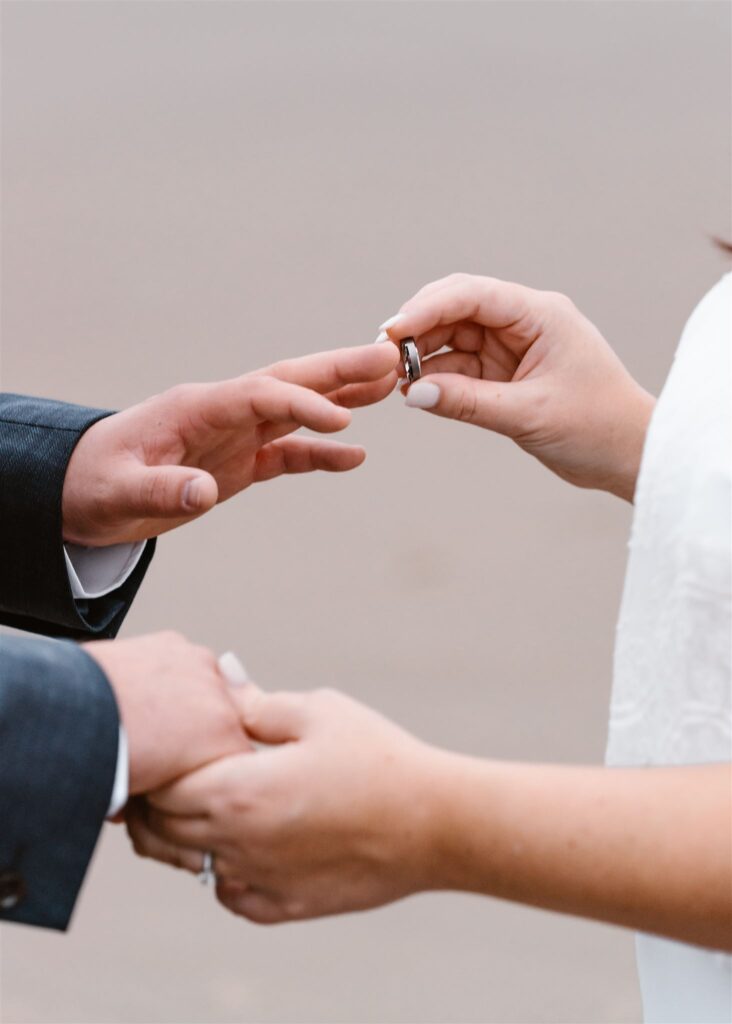 a close up shot of a bride placing the wedding band on her grooms finger