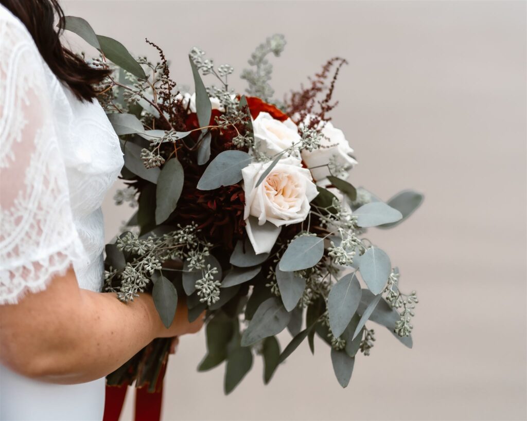 a detail shot of the brides romantic bouquet. It is is filled with white, red, and merlot colored roses. Soft greenery adds depth to this romantic arrangement.