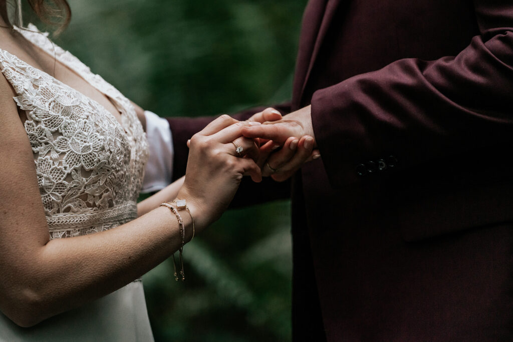A bride places a wedding band on her grooms hand during their forest wedding
