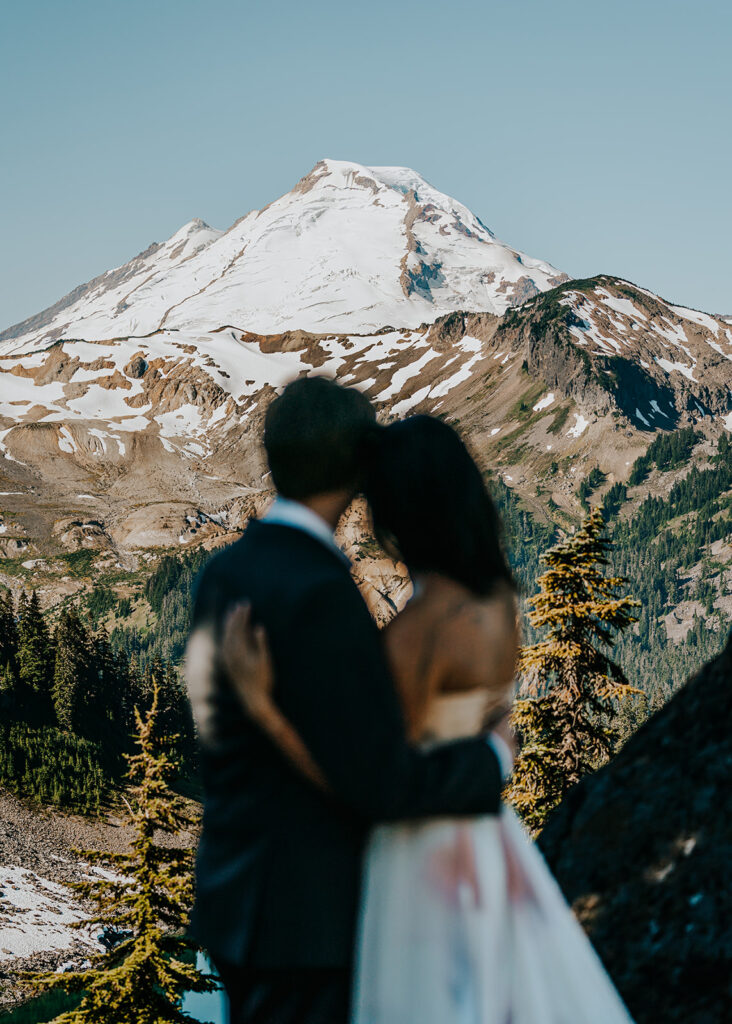 a blurry couple in their wedding attire frames a sharp mount baker