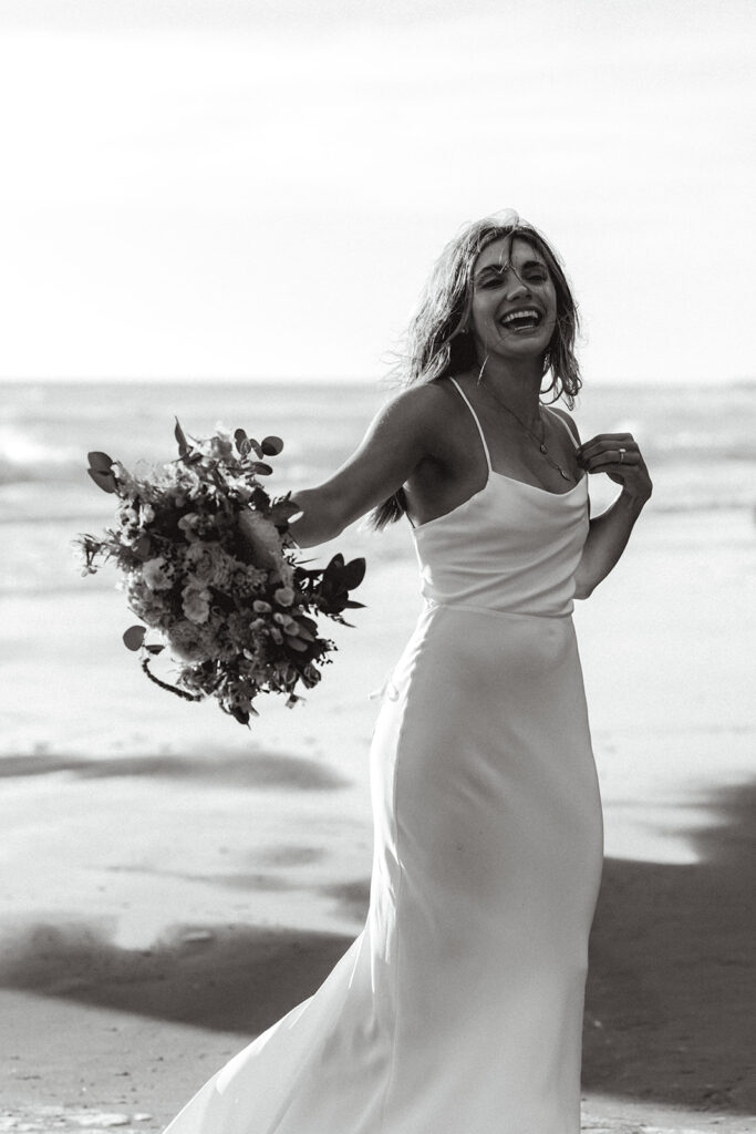 a black and white image of a bride twirling with her bouquet smiling widely 