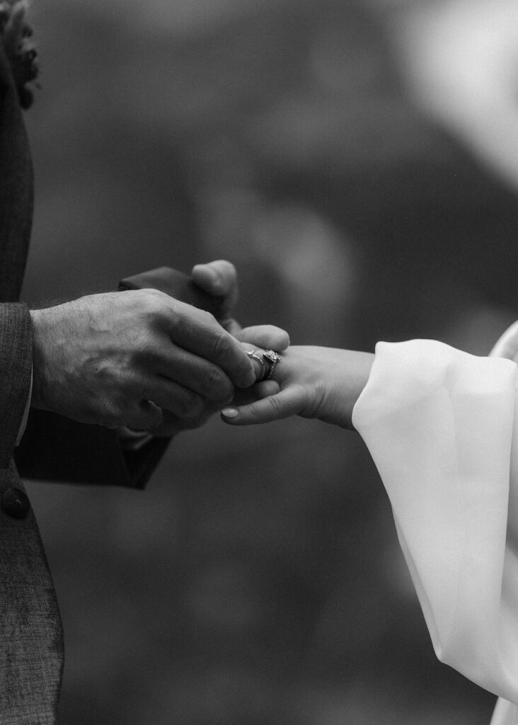 a close up shot of a groom slipping on his brides wedding ring
