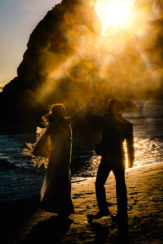 after they decided how to elope, a couple dances on a rocky beach. ambient sunlight and solar flares create a mystical and romantic glow for the scene