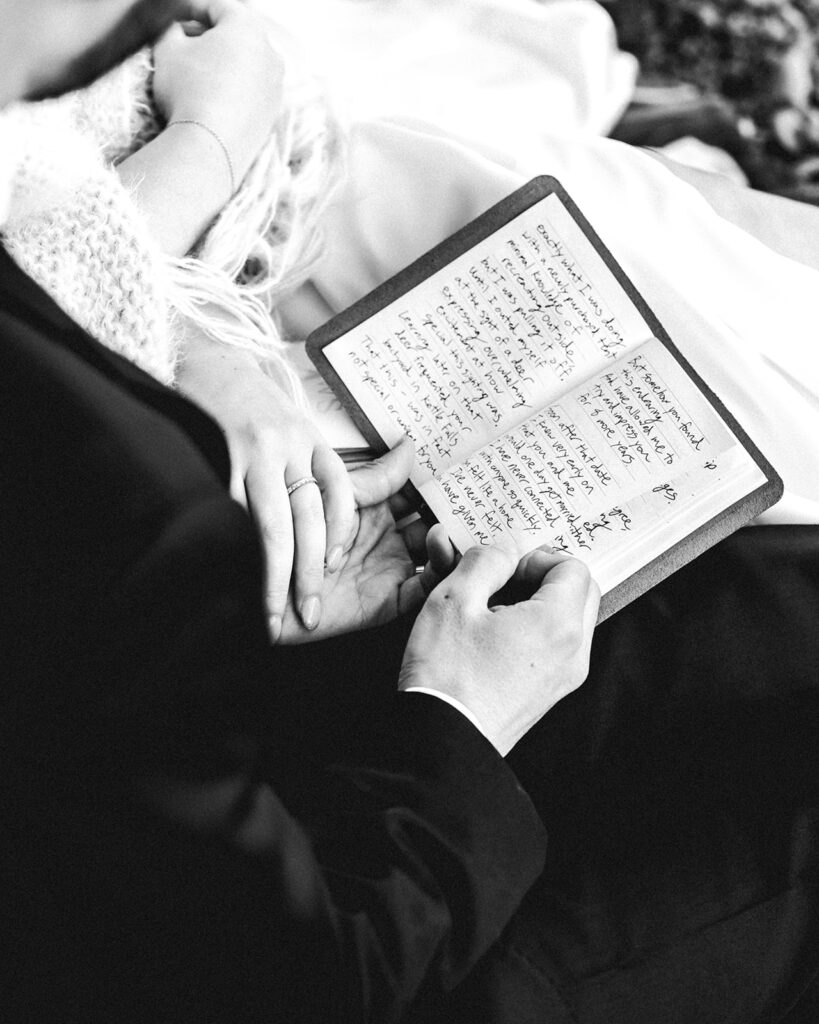 a close up shot of a vow book, held by the groom, his bride holds his hand as he reads his vows 