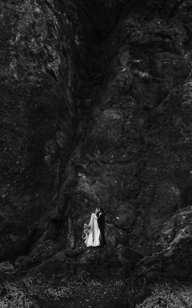 after they decided how to elope, a bride and groom kissing on top of a basalt rock. the image is black and white, putting an emphasis on the negative space of the landscape 