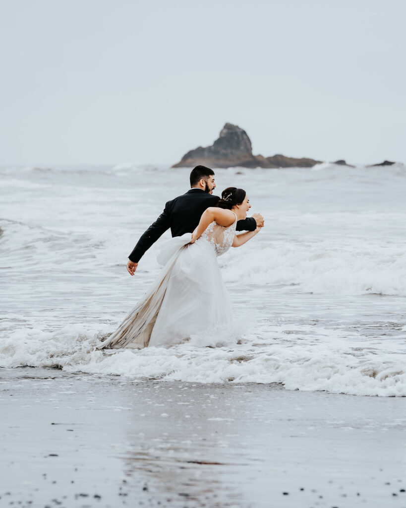 after they decided how to elope, a bride and groom send it into the icy pacific. their smiles are wide as the waves roll over their feet