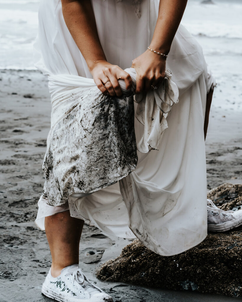 a close up shot as a bride wrings out the ocean water from her dirty dress