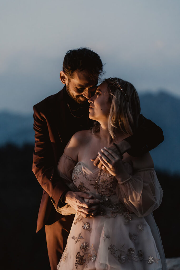 after learning how do you elope a couple snuggle in the twilight hour embracing in their wedding attire. Golden light from a lantern illuminates their faces