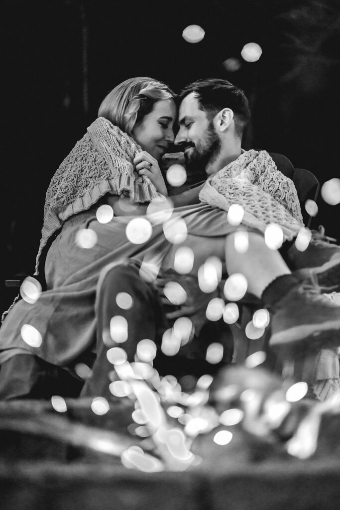 after they decided how to elope, a couple snuggles up in front of a campfire to end their day. the bride sits in her grooms lap as they press their foreheads together