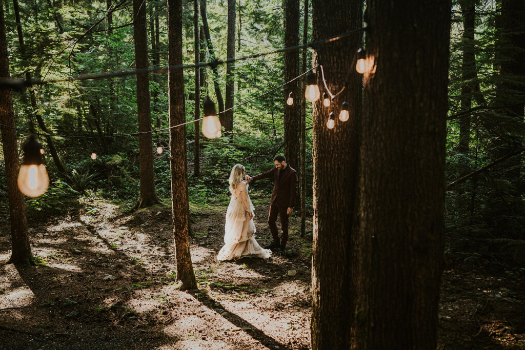 a landscape shot of a first look taken from a slightly higher up perspective. a couple stands in a forrest as they gaze lovingly at each other admiring their partners attire
