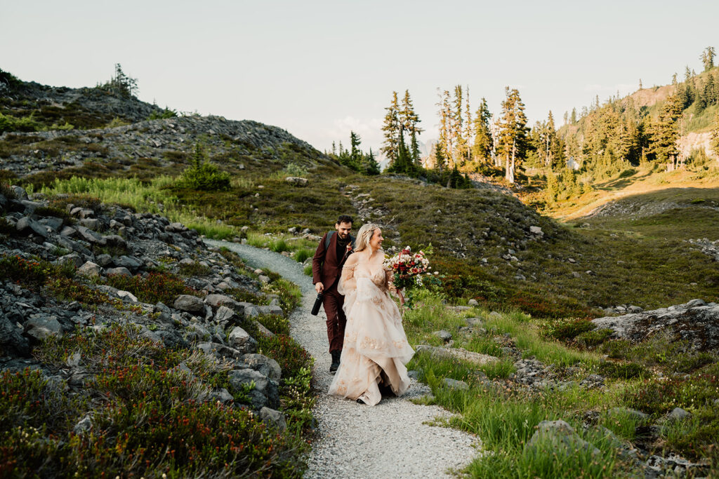 a bride and groom explore a beautiful green landscape, speckled with wildflowers during their mount baker elopement