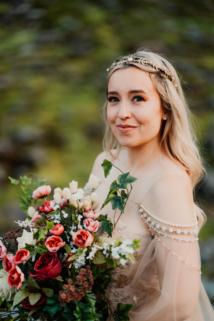a bride smiles softly at the camera as she holds here bouquet