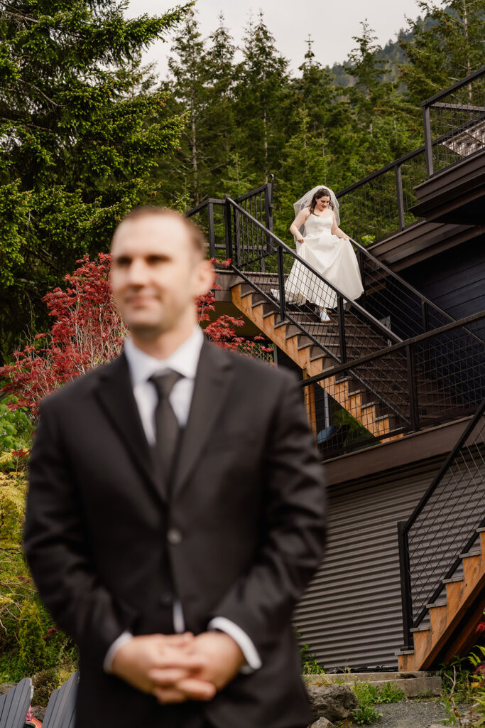 a bride makes her way down the stairs for a first look. She is framed by the silhouette of her groom, waiting for her during their lake crescent wedding. 