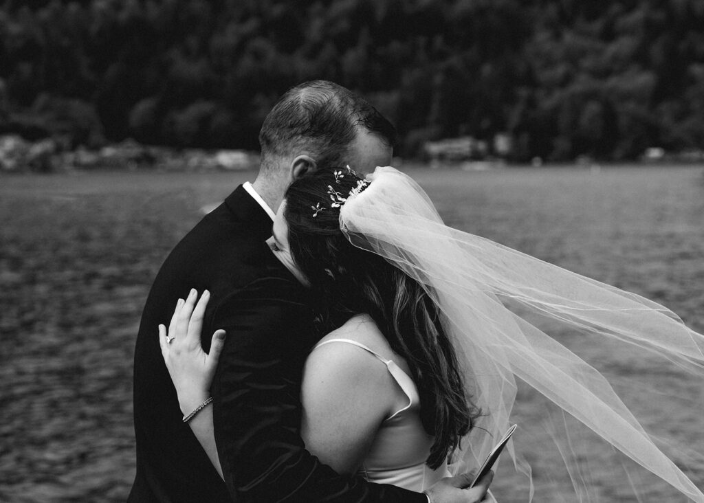 a black and white image of the bride and groom from this lake crescent wedding embracing. The wind blows gently through her veil.