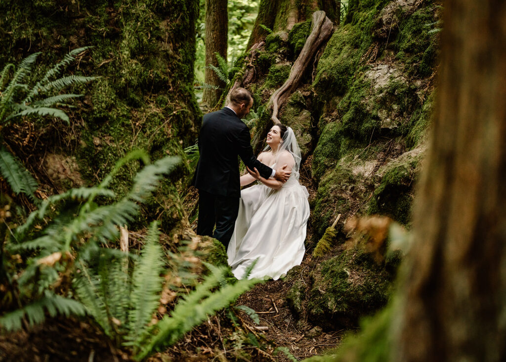 a bride and groom snuggle in an area filled with mossy rocks. They smile lovingly at each other and take in the moment alone before their Lake Crescent wedding