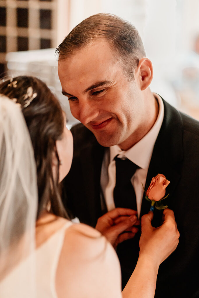 a bride gently fastens her grooms boutonniere as he gazes lovingly at her before their lake crescent elopement 