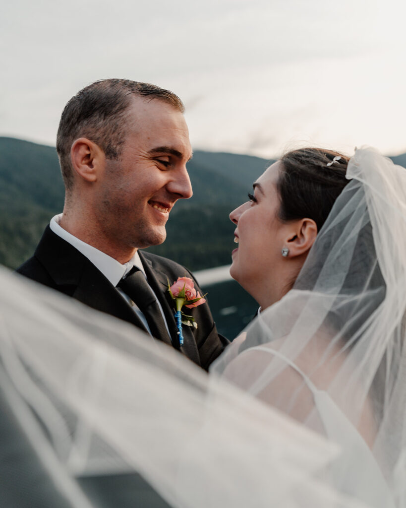 a bride and groom smile widely at each other. they are framed by the swoop of her veil 