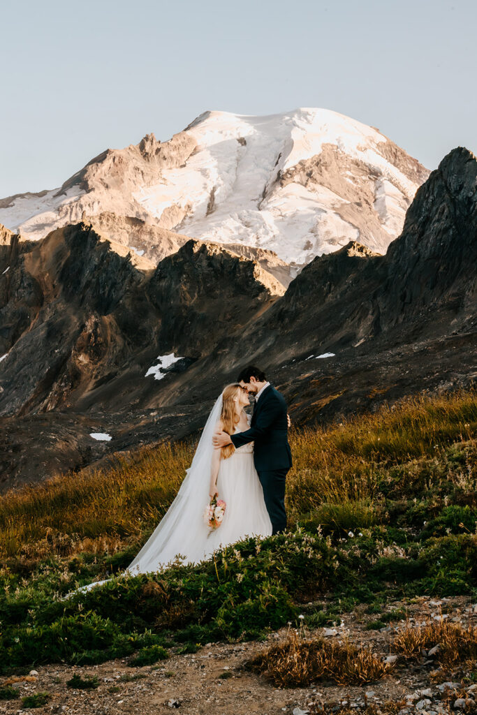 a bride and groom embrace in front of a striking mount baker during golden hour
