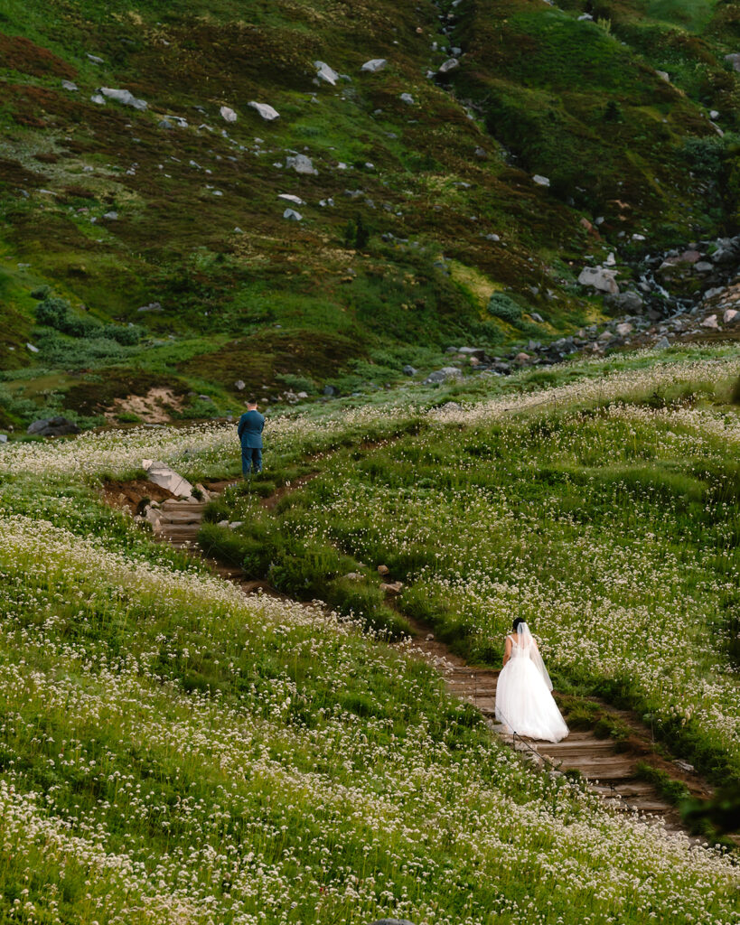 a groom stands in a field of wildflowers as his bride walks up to him for their first look