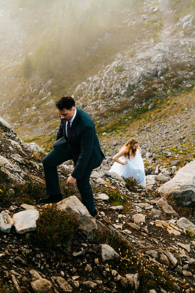 an overhead shot of a bride and groom hiking in their wedding attire during their last minute elopement. The clouds can be seen rolling in below them