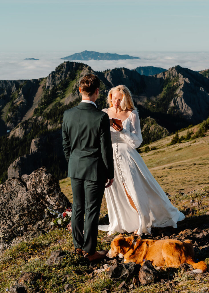a bride reads her vows as her dog rests at her feet. she smiles sweetly at her groom