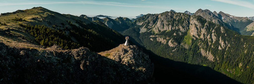 a panoramic shot of the mountains during this Olympic Peninsula elopement. Our couple stands center of the shot on a cliff.