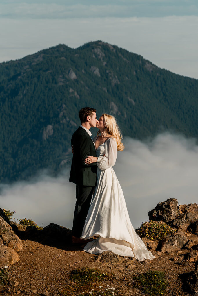 A bride and groom kiss as mountains tower behind them 