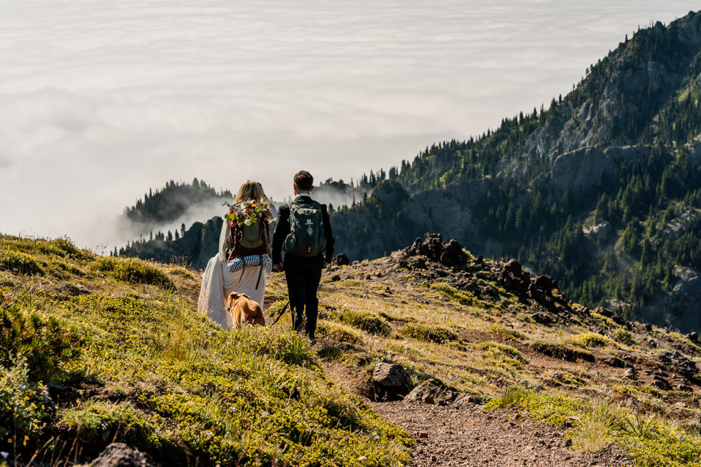 a bride and groom hike and explore the Olympic peninsula mountains. they wear hiking backpacks and we see the brides bouquet fastened to the outside of her pack