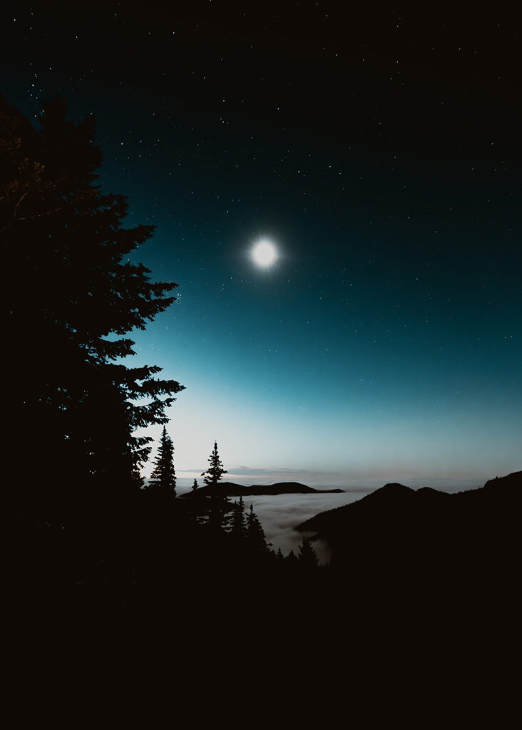 a bright moon illuminates a cloud inversion forming in the start of blue hour