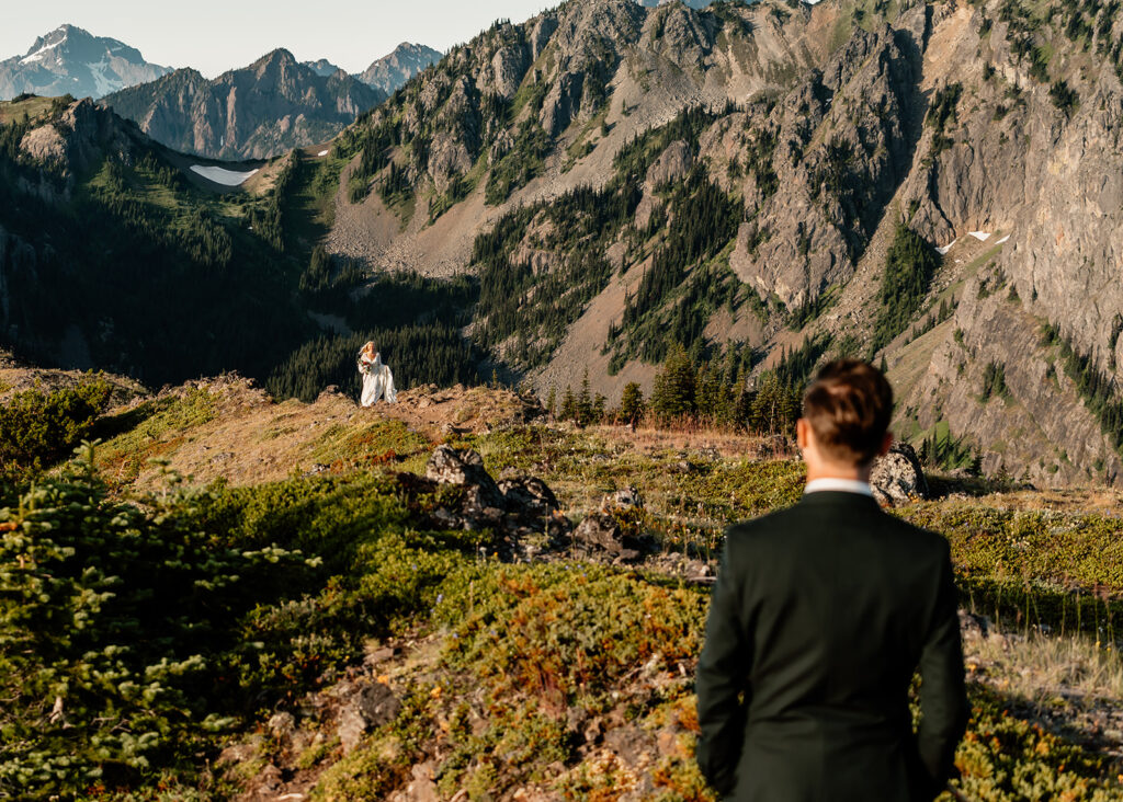 an over the shoulder shot of the landscape in front of the groom. We see his bride walking up over the peak for their first look during this Olympic Peninsula elopement. 