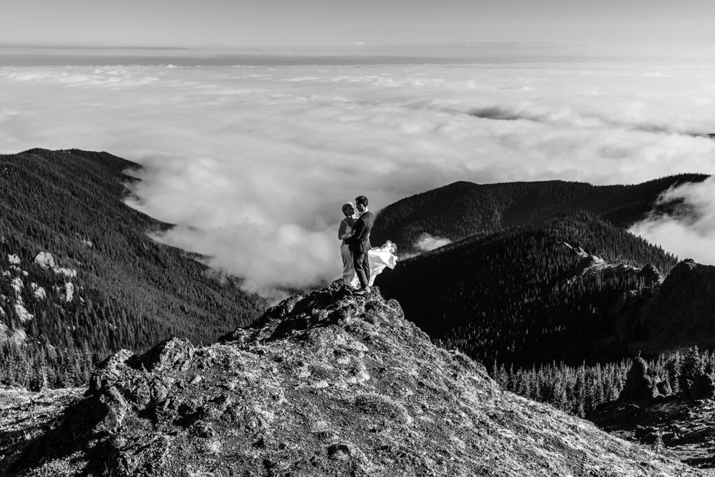 a black and white image of a couple embracing with a cloud inversion sweeping below them during their Washington elopement 