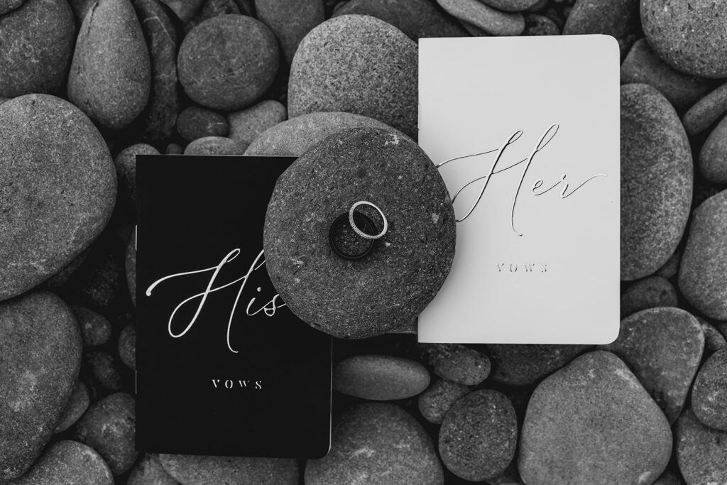 a black and white image of vow books and wedding bands from an Olympic National Park wedding, places on tumbled beach rocks 