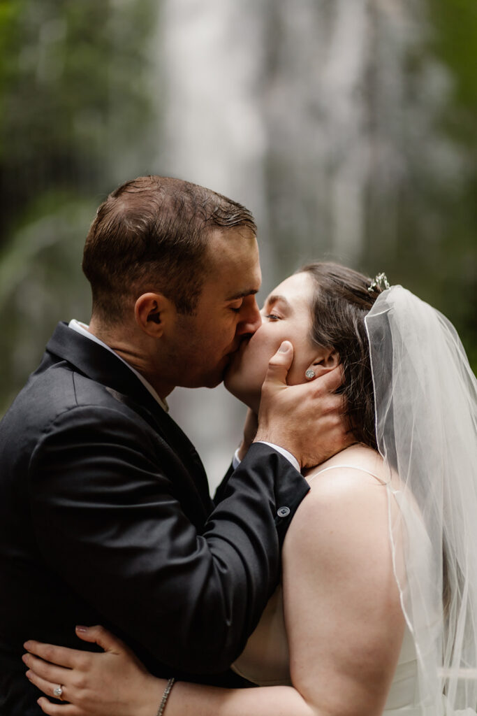 a bride and groom kiss in front of a misty waterfall