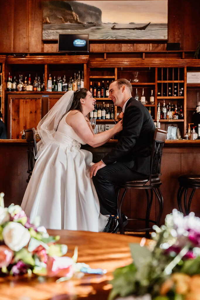 a bride and groom sit at a bar together and smile widely at each other during their Olympic National Park wedding 