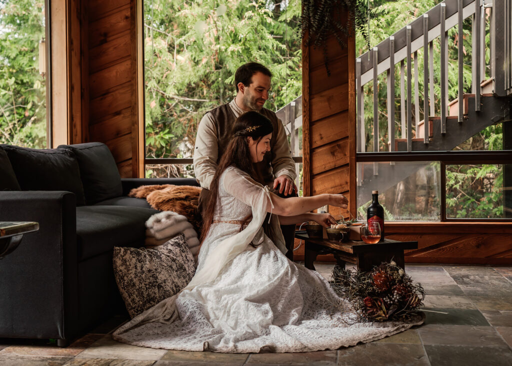 A couple in their wedding attire share a meal in their lodging 