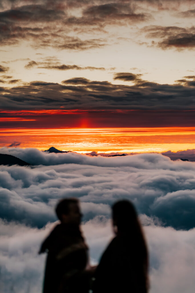 The shadowed silhouette of a couple embracing frames an unbelievable cloud inversion in the Olympic Mountains during sunset 
