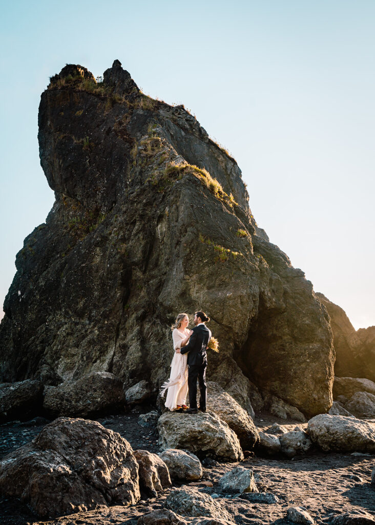 During their Olympic National Park wedding a couple embraces on a rocky formation on ruby beach. they are highlighted by golden sunlight as the sunset begins